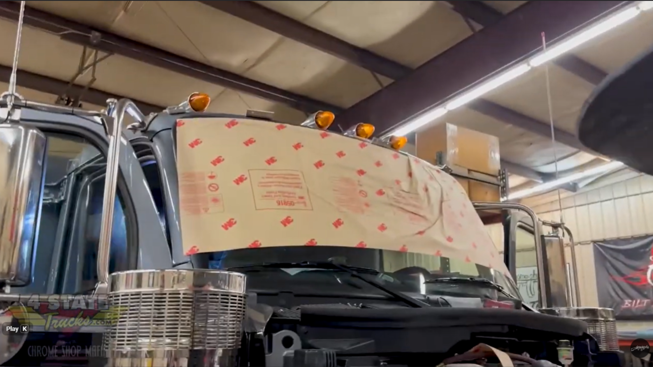 Custom sun visor mounting brackets installed on flat roof Peterbilt 589 cab during fabrication process inside shop.