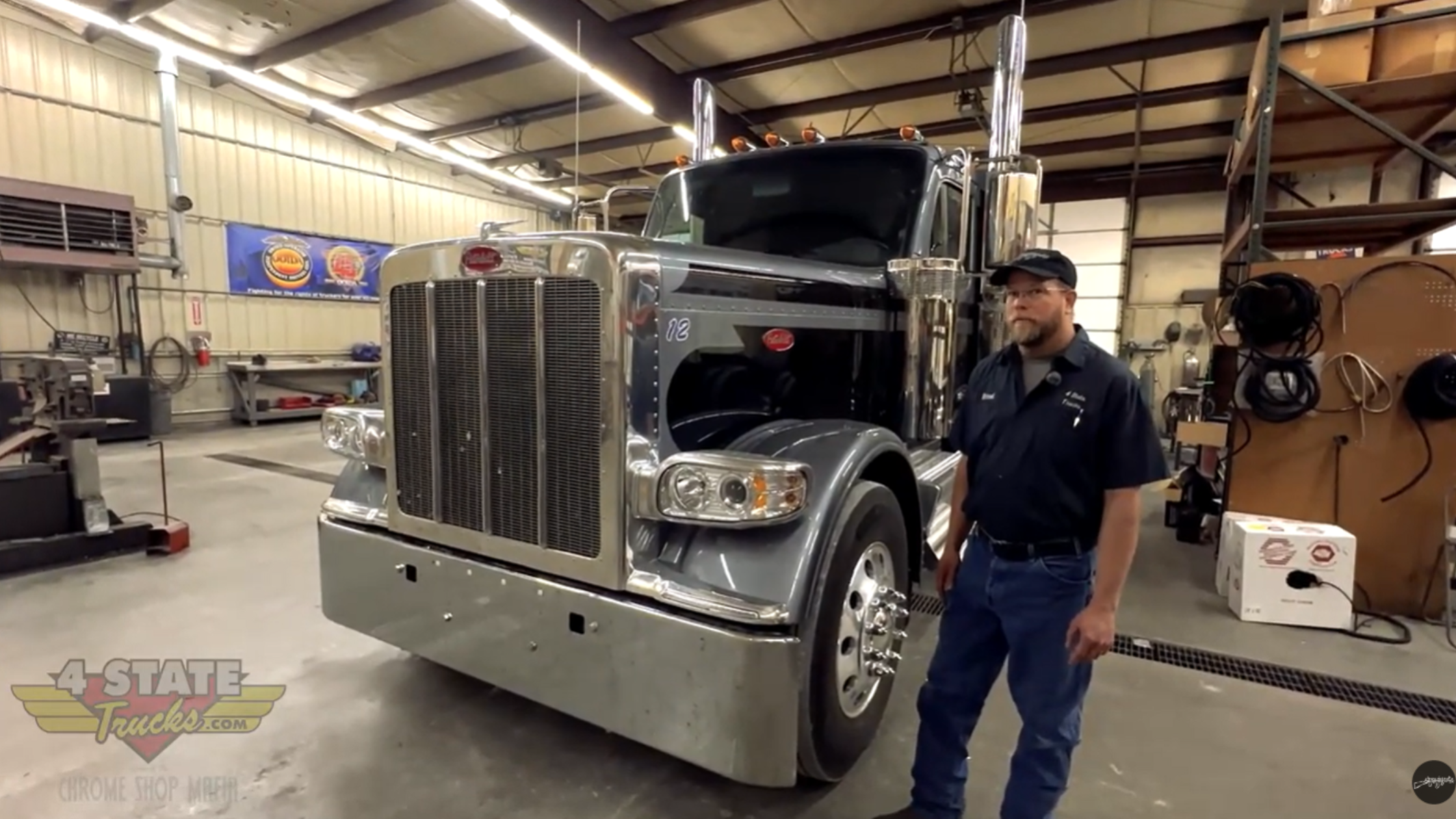 Front view of flat roof Peterbilt 589 inside Chrome Shop Mafia shop with technician standing beside grille and factory bumper before custom modifications.