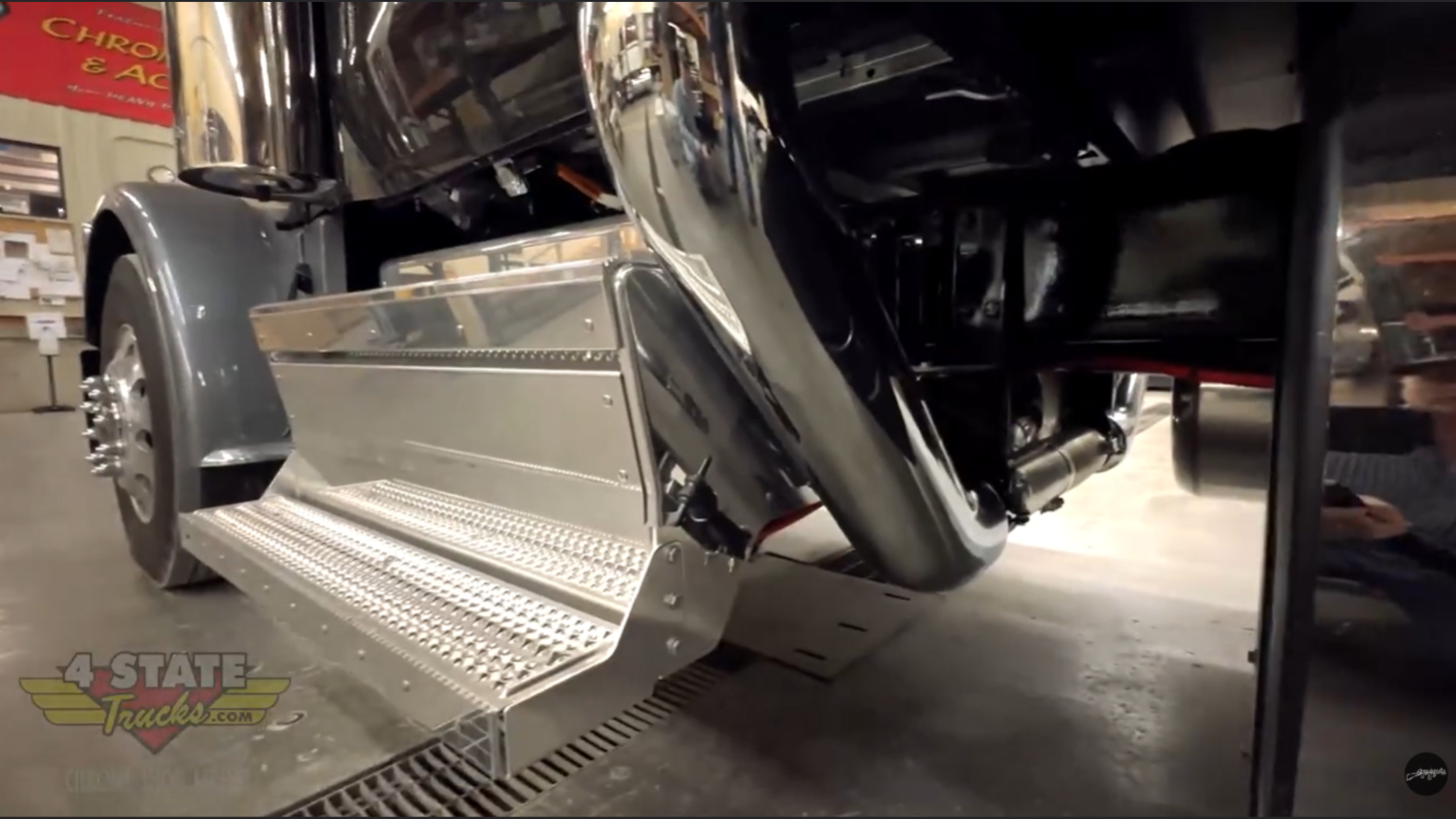 Close-up of Peterbilt 589 lower step and cab mount area showing curved body lines and custom stainless step panel inside installation shop.