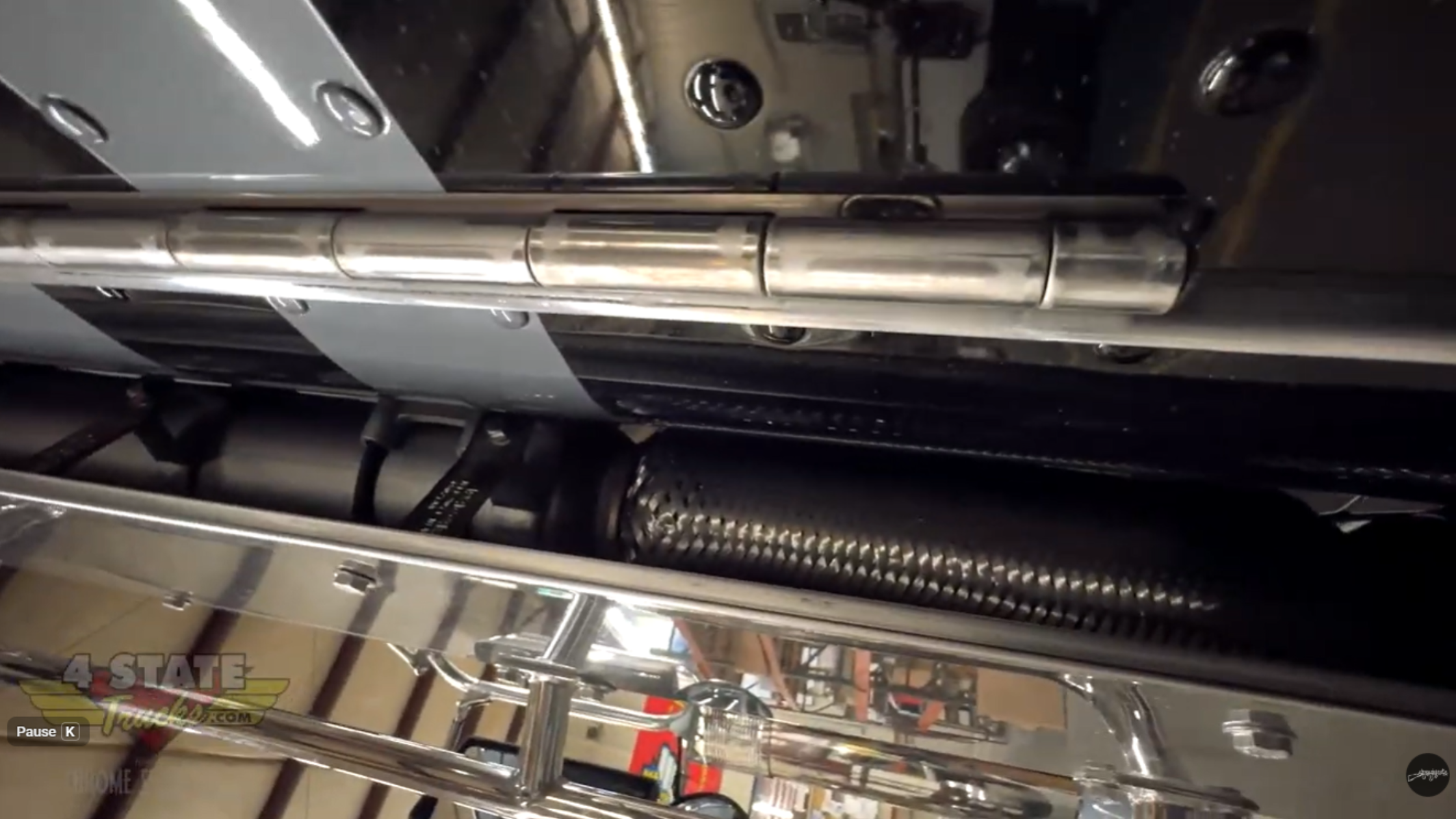 Factory exhaust flex pipe and mounting system on Peterbilt 589 showing frame-mounted elbow and cab-mounted upper pipe inside shop.